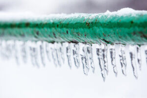 Frozen water pipe that may burst. The green water pipe is covered with ice