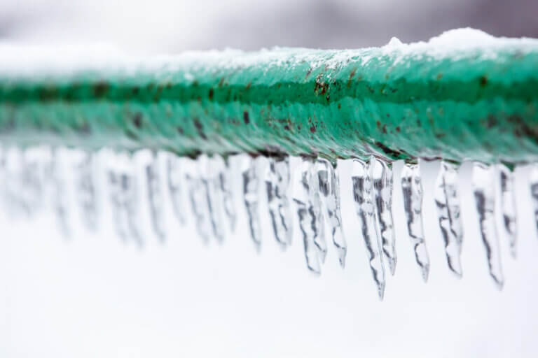 Frozen water pipe that may burst. The green water pipe is covered with ice