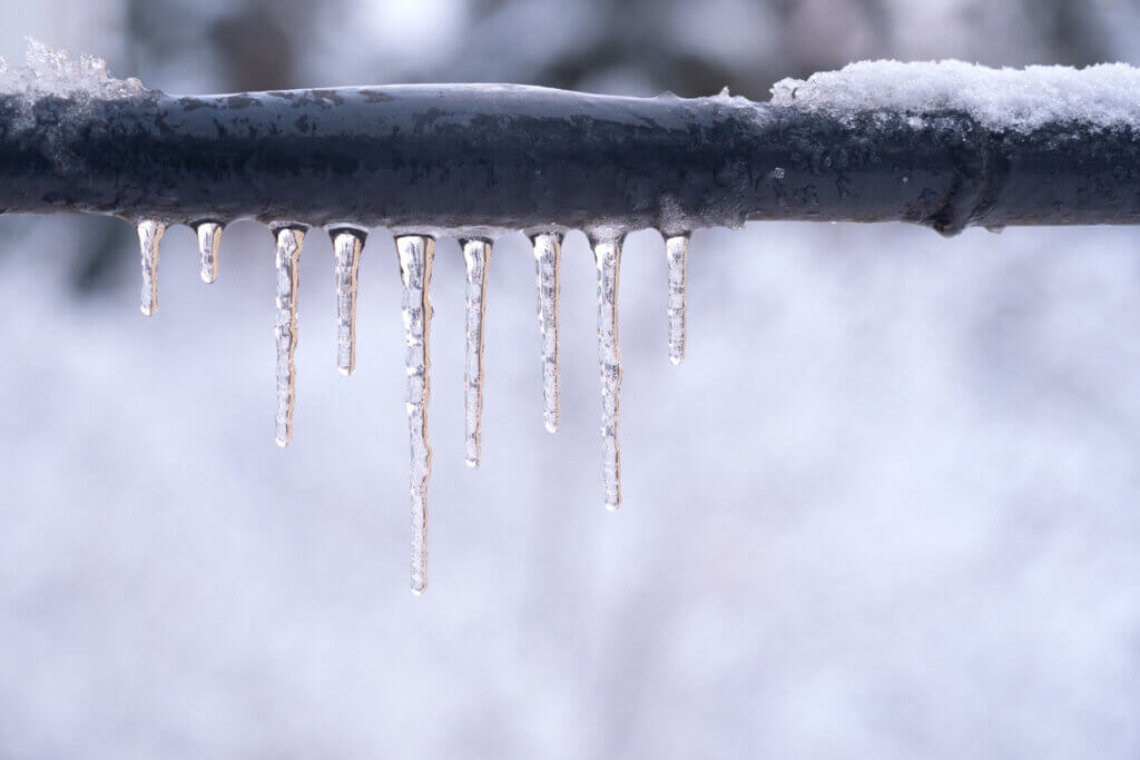 Frozen icicles on a gray pipe after a thaw in winter.