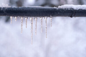 Frozen icicles on a gray pipe after a thaw in winter.