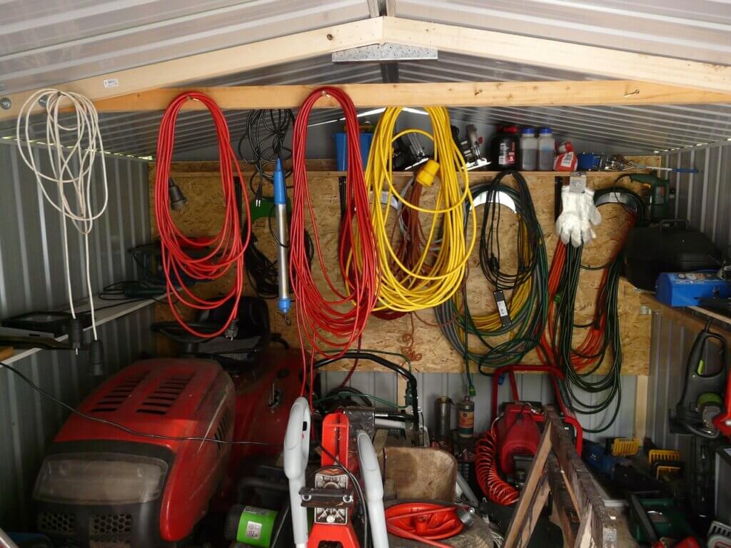 a garage / storage space with many objects including a lawn mower, and cables.